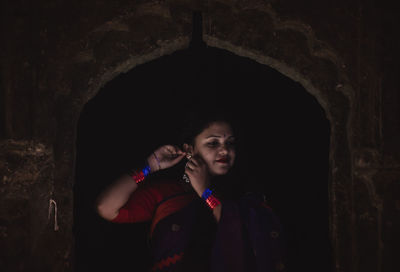 Portrait of woman standing against dark wall