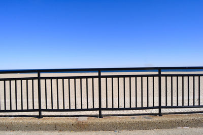 Railing on field against clear blue sky