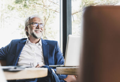 Smiling mature businessman sitting at table in a cafe with laptop