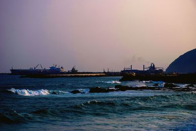 Boats sailing in sea against clear sky during sunset