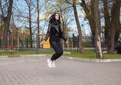 Full length of young woman on footpath by trees