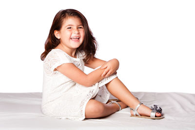 Portrait of smiling girl sitting on bed against white background