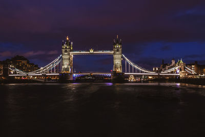 Illuminated bridge over river against sky at night