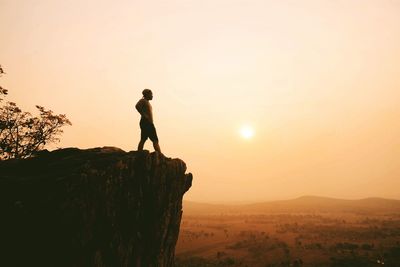 Silhouette of man with arms outstretched against sunset sky