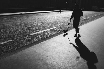 Silhouette man walking with dog on sidewalk