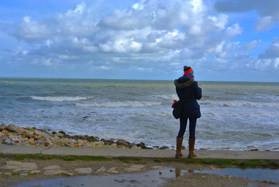 Rear view of man standing on beach against cloudy sky
