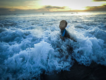 Man in sea against sky during sunset