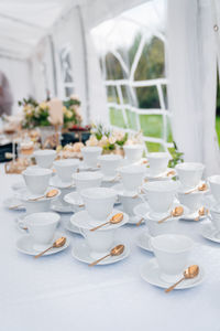 Close-up of white teacups with gold spoons prepared for the event.