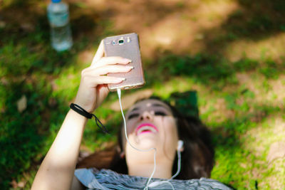 Young woman using phone while lying down on field