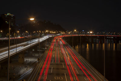 High angle view of light trails on road by river in city at night