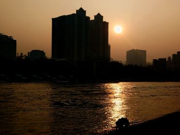 Silhouette buildings by city against sky during sunset