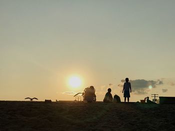 Silhouette people on beach against sky during sunset