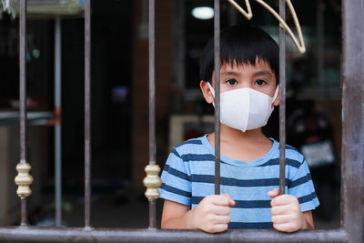 Asian boy in a detained face standing looking out of the house distancing to prevent covid 19 