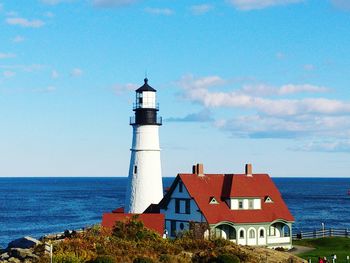 Lighthouse by sea against blue sky