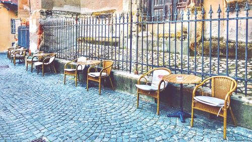 Empty chairs and tables on sidewalk cafe amidst buildings in city