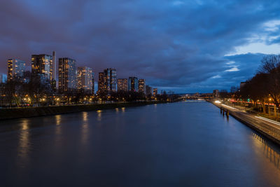 Illuminated buildings by river against sky at dusk