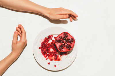 The woman's hands are lying on a white table next to a plate with a sliced juicy pomegranate.