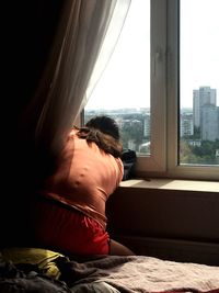 Rear view of woman looking through window at home