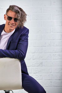 Portrait of a smiling young man sitting against wall