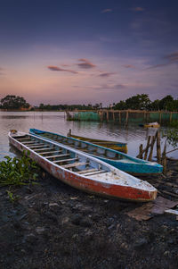 Boat moored on shore against sky during sunset