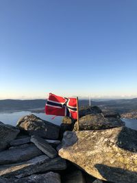 Scenic view of flag on rocks against clear blue sky