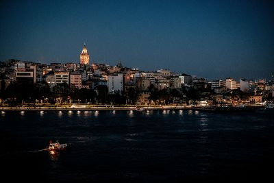 Illuminated buildings by river against blue sky at night