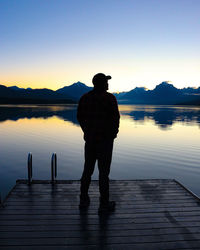 Rear view of man walking on pier over lake against clear sky