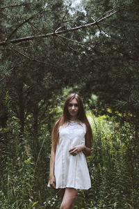 Young woman standing against trees in forest