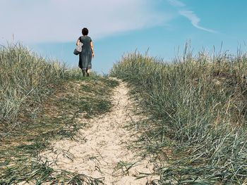 Rear view of man walking on field against sky