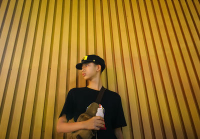 Boy looking away while standing against corrugated wall