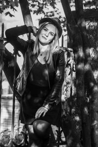 Portrait of smiling young woman standing by tree at park