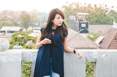 Young woman using mobile phone while standing against trees