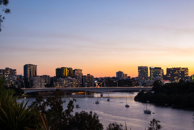 River by illuminated buildings against sky during sunset