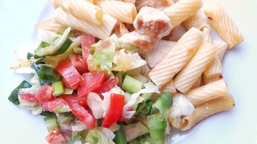 Top view close-up of tortiglioni noodles with chicken meat and iceberg mixed lettuce salad.