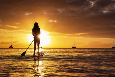 Silhouette man standing in sea against sky during sunset