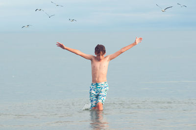 Rear view of shirtless man in sea against sky