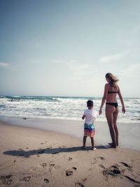 Rear view of girl standing at beach against sky