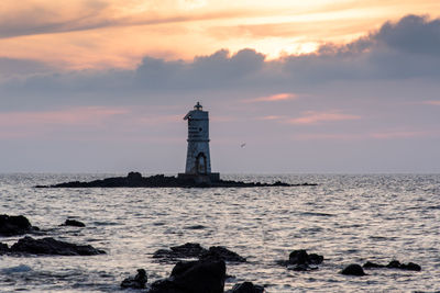 Lighthouse by sea against sky during sunset