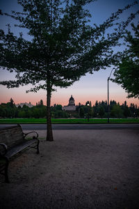 Park bench by trees against sky during sunset