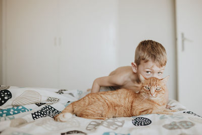 Boy kissing ginger cat on bed at home
