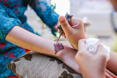 Cropped image of beautician making henna tattoo on woman hand