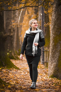Full length of young woman walking along autumn trees