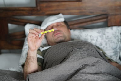 Man checking temperature while lying on bed at home