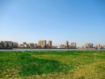 Scenic view of field by buildings against clear sky