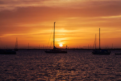 Silhouette sailboats in sea against sky during sunset