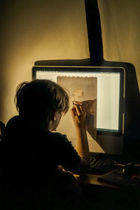 Rear view of a kid drawing on the computer