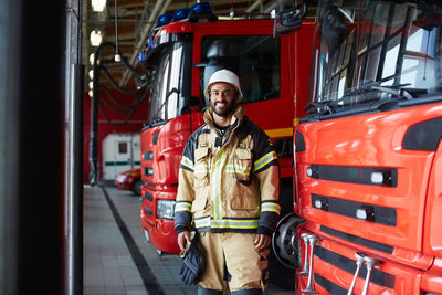 Portrait of smiling firefighter standing by fire engine at fire station