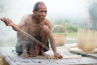 Shirtless man making wicker basket