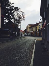 Empty road by buildings in city against sky