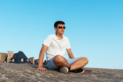 Young man sitting on sunglasses against clear blue sky